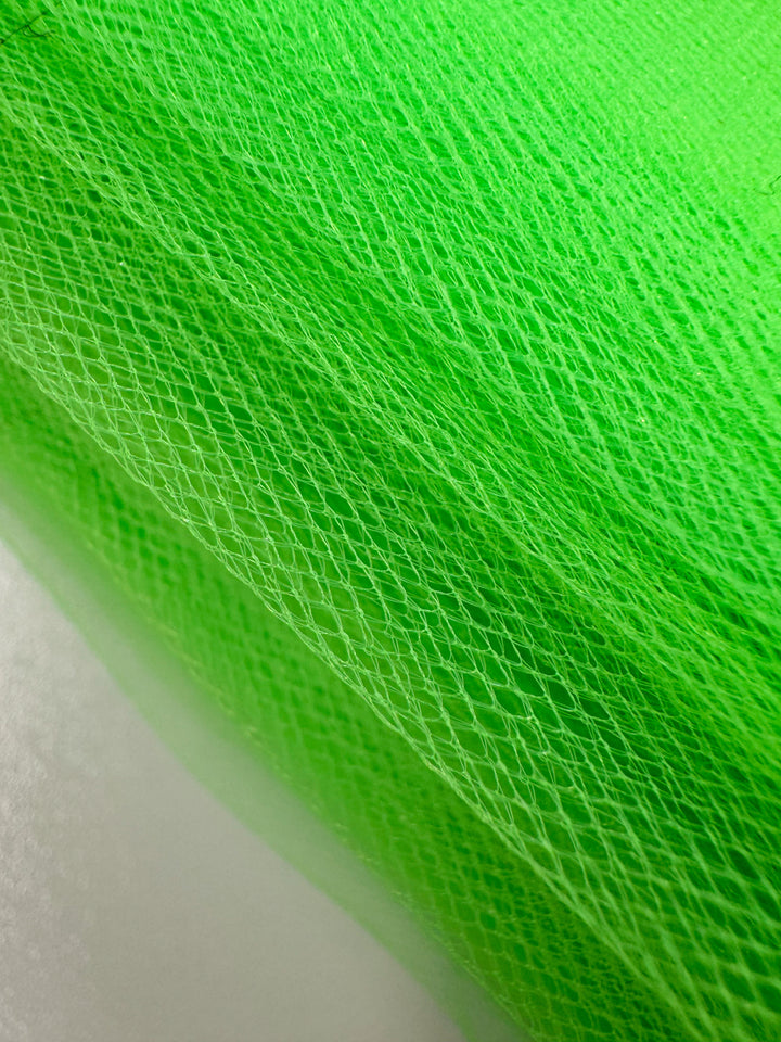 Close-up of Super Cheap Fabrics' Soft Tulle - Neon Lime (150cm), featuring a diamond-shaped pattern and textured, layered look. Ideal for costumes or veils, with a softly blurred light gray and green background.