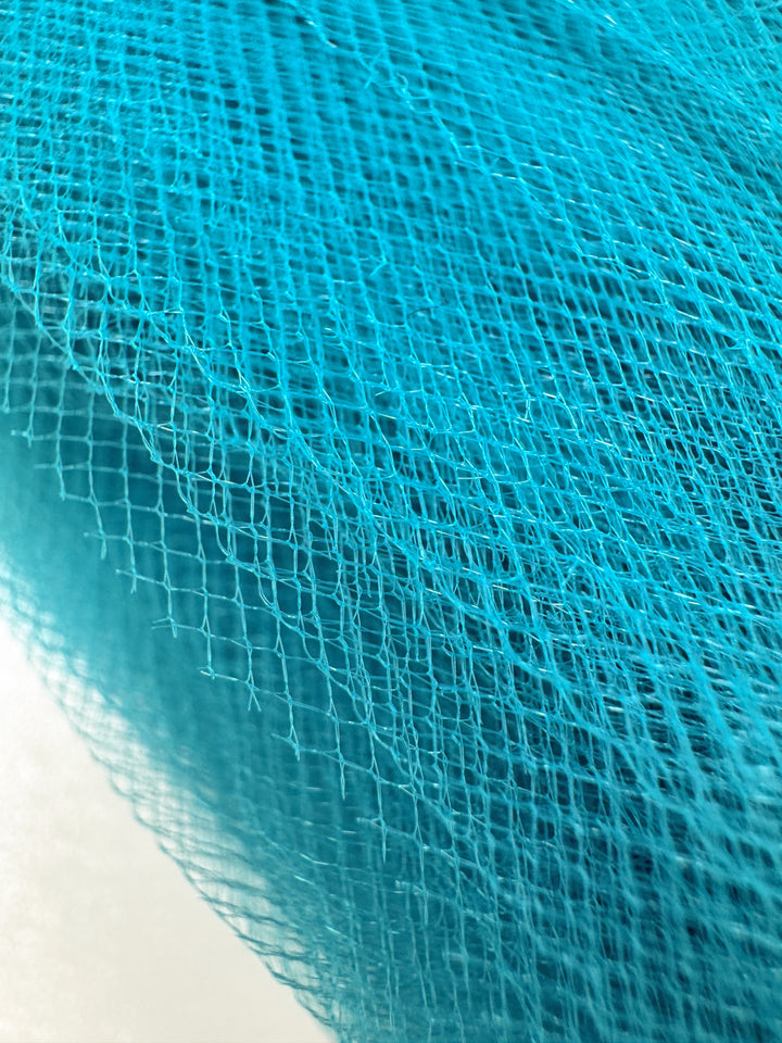 Close-up of Super Cheap Fabrics’ Soft Tulle - Lake Blue (150cm): this translucent fabric features a grid pattern and fine threads, creating layered depth—ideal for craft projects or bridal veils.