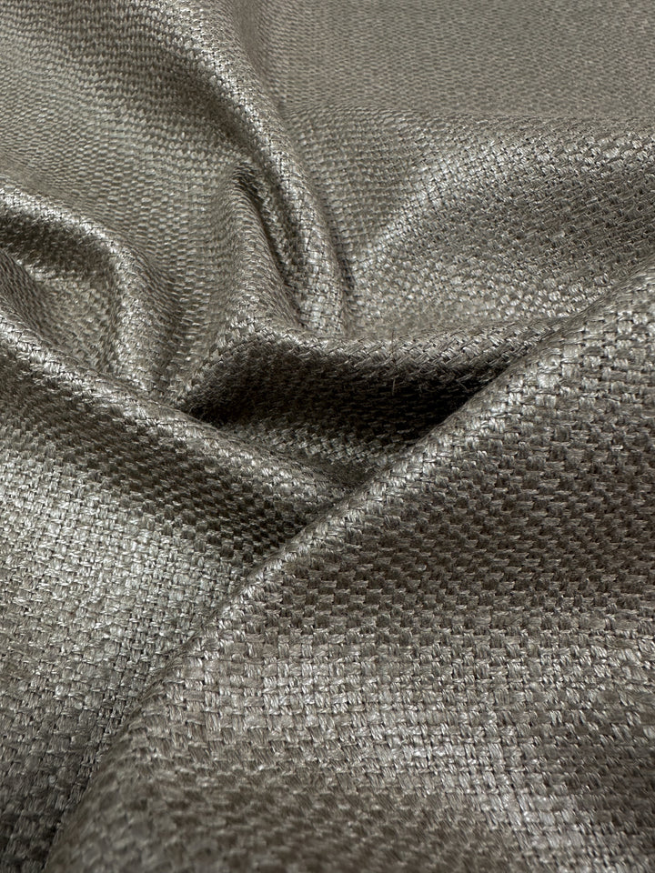 This close-up showcases the 'Upholstery Basket Weave - Dorian Putty - 145cm' by Super Cheap Fabrics, featuring metallic silver fabric with a textured basket weave. The heavyweight material drapes in gentle folds, beautifully highlighting its shiny, reflective surface.