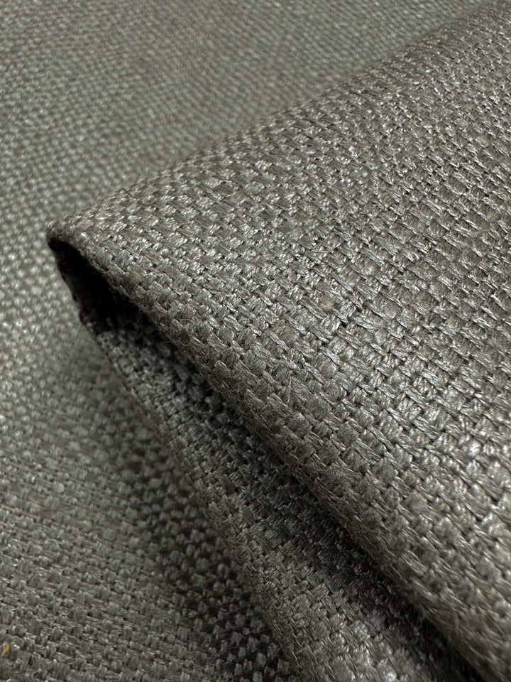 Close-up of folded Upholstery Basket Weave - Dorian Putty fabric by Super Cheap Fabrics. It features a textured, thick basket weave pattern in light and dark grey tones, offering a slightly reflective surface for striking contrast. Width: 145cm.