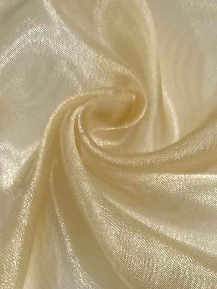 A close-up of Super Cheap Fabrics' Organza - Fall Leaf - 150cm shows soft, shimmery ivory sheer fabric swirled in a spiral, highlighting its smooth texture and subtle sheen.