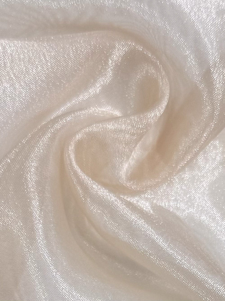 Close-up of Organza - Croissant - 150cm by Super Cheap Fabrics, showing its soft, shimmery light beige sheer fabric with smooth swirling texture and gentle folds that reflect light for a delicate, elegant look.