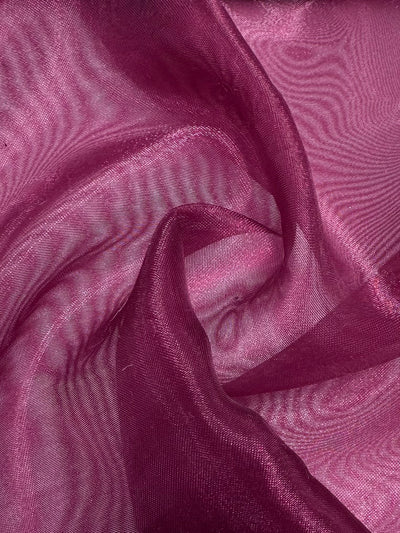 A close-up of Super Cheap Fabrics' Organza - Red Bud - 150cm shows sheer, magenta-red fabric with a soft, flowing texture, gentle folds, wavy patterns, and a subtle sheen.