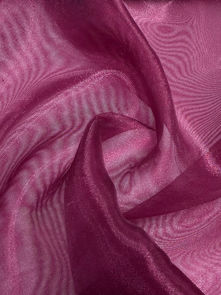 A close-up of Super Cheap Fabrics' Organza - Red Bud - 150cm shows sheer, magenta-red fabric with a soft, flowing texture, gentle folds, wavy patterns, and a subtle sheen.