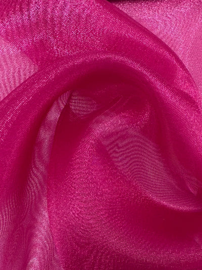 A close-up of Super Cheap Fabrics' Organza - Very Berry (150cm), showing sheer, shimmery pink fabric draped in soft folds that create a wavy, textured pattern with elegant highlights and shadows.