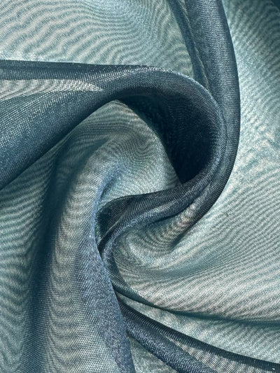 Close-up of Super Cheap Fabrics' Organza in Teal (150cm), showing its smooth, lightweight texture gently twisted, with folds and curves creating elegant shadows and highlights on the sheer material.