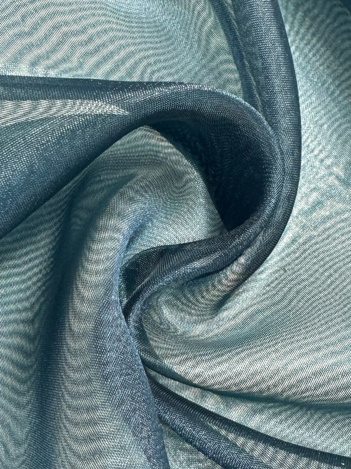 Close-up of Super Cheap Fabrics' Organza in Teal (150cm), showing its smooth, lightweight texture gently twisted, with folds and curves creating elegant shadows and highlights on the sheer material.