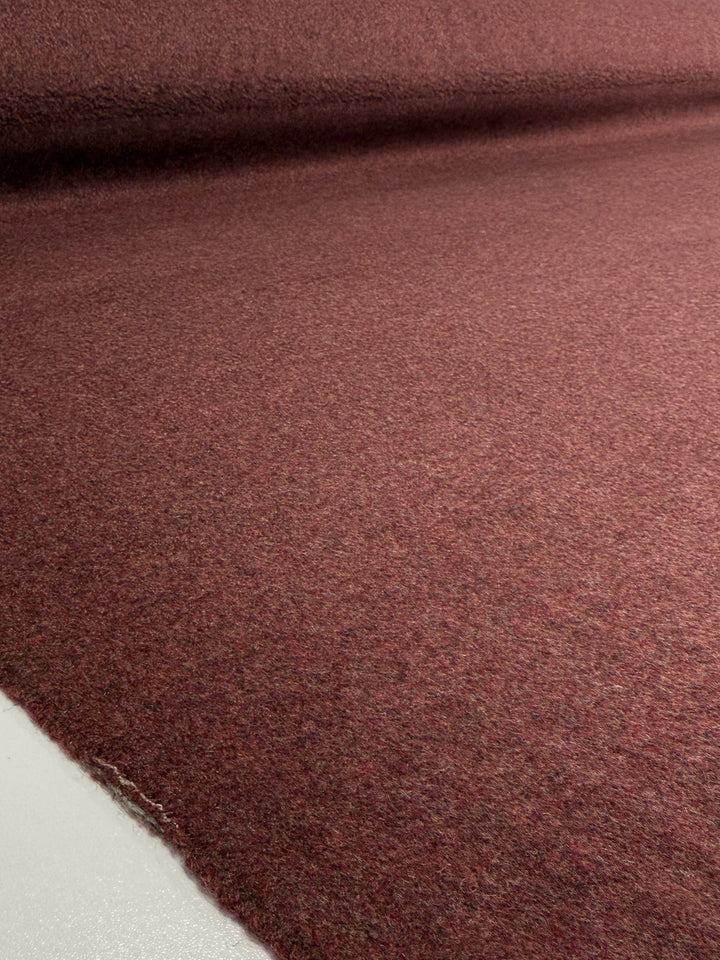 A close-up of Super Cheap Fabrics' Wool Cashmere - Marsala Marle (150cm) showcases its soft, textured reddish-brown surface as the heavy weight fabric unrolls across a white background.