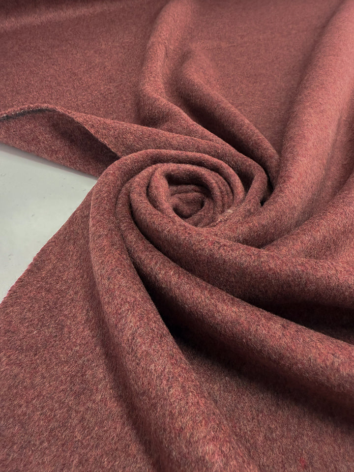A close-up of Super Cheap Fabrics' Wool Cashmere - Marsala Marle (150cm), showcasing its soft, textured reddish-brown material arranged in a spiral on a flat surface.