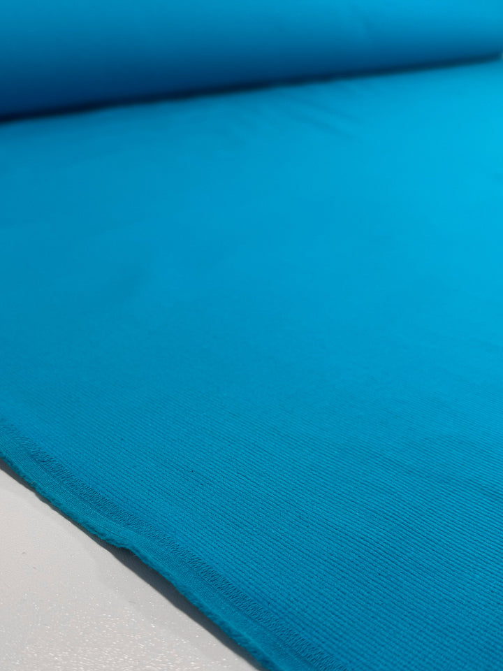 A close-up of Super Cheap Fabrics' Pin Wale Corduroy in Blue Jewel (147cm) unrolled, showcasing its smooth ribbed texture and tidy edge.