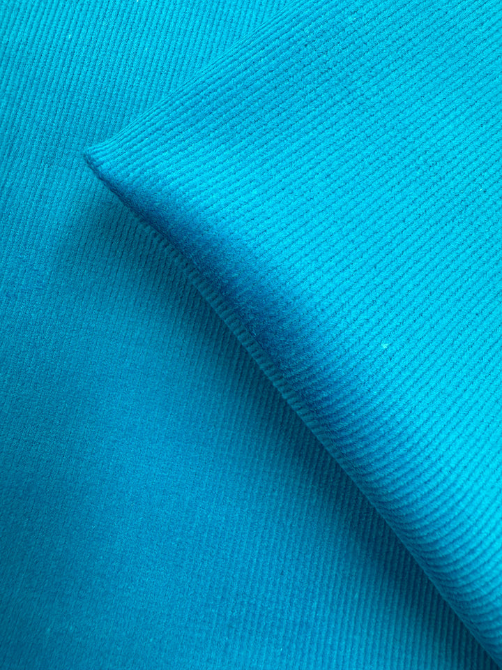 Close-up of Super Cheap Fabrics' Pin Wale Corduroy - Blue Jewel (147cm), showing two pieces overlapping with fine vertical ribs and a smooth, soft blue texture.
