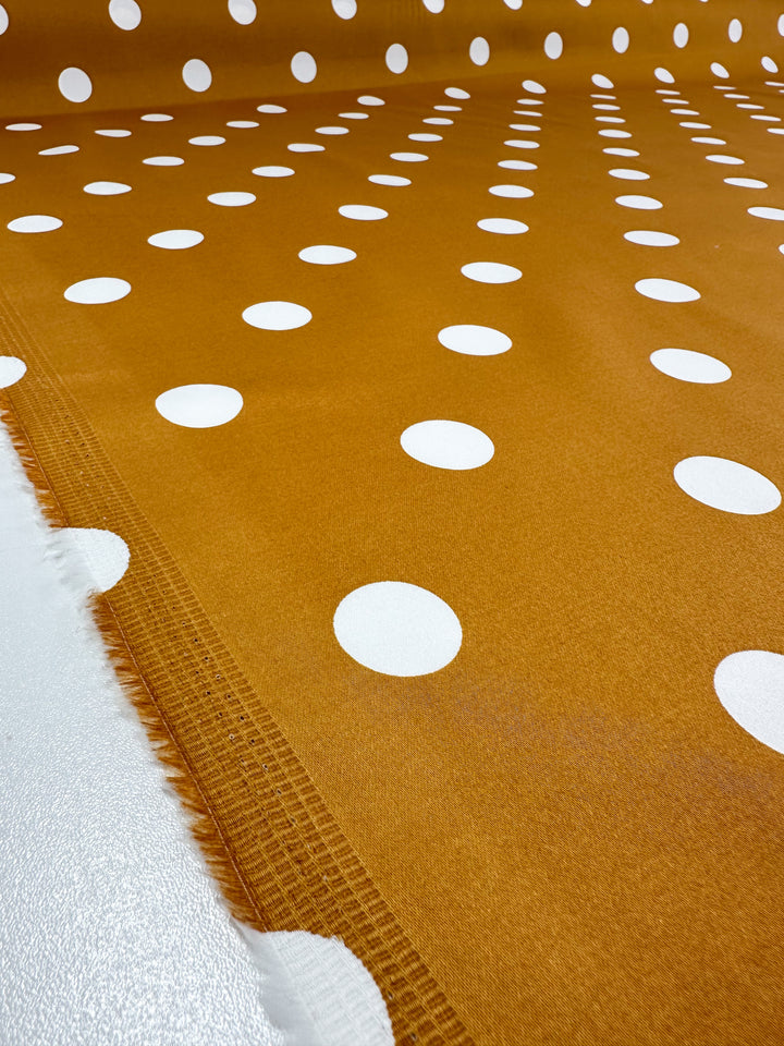 A soft Cotton Sateen by Super Cheap Fabrics, named Polka Yam, features a brown background with evenly spread white polka dots. This 125cm wide fabric is visible along the edge and ideal for crafting elegant dresses.