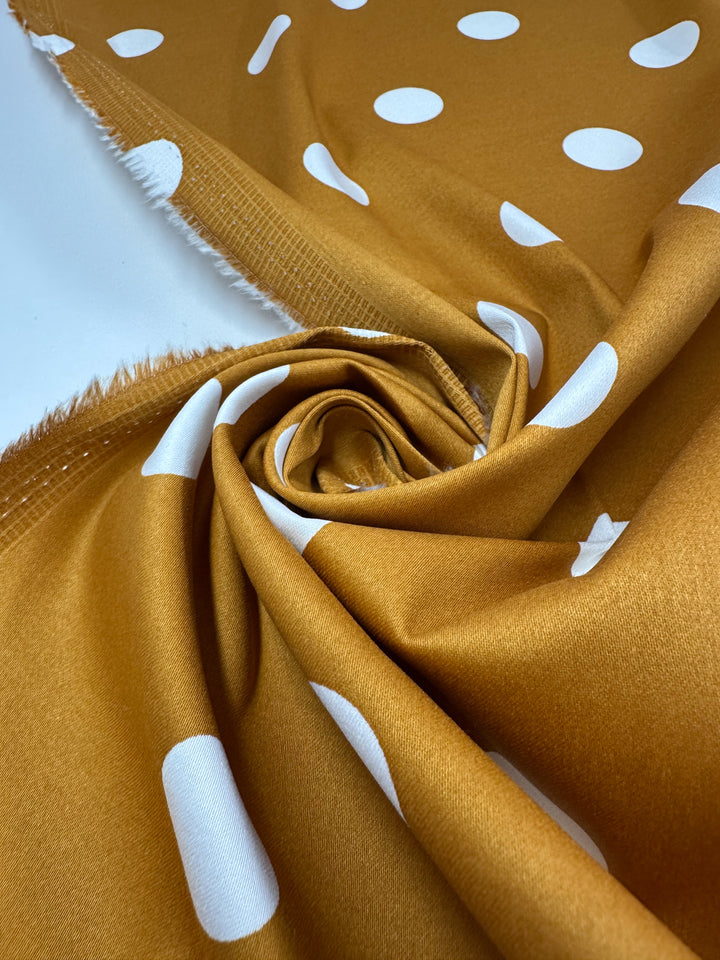The "Polka Yam" rust-colored Cotton Sateen by Super Cheap Fabrics features large white polka dots in a circular spiral pattern. Measuring 125cm wide, it's perfect for crafting playful dresses with its visible slightly frayed edges.