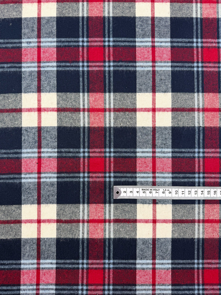 A close-up of Flannel Tartan - Highland (Super Cheap Fabrics), a medium weight cotton in red, navy, white, and gray plaid, with a white centimeter ruler for scale near the bottom right; fabric width is 145cm.