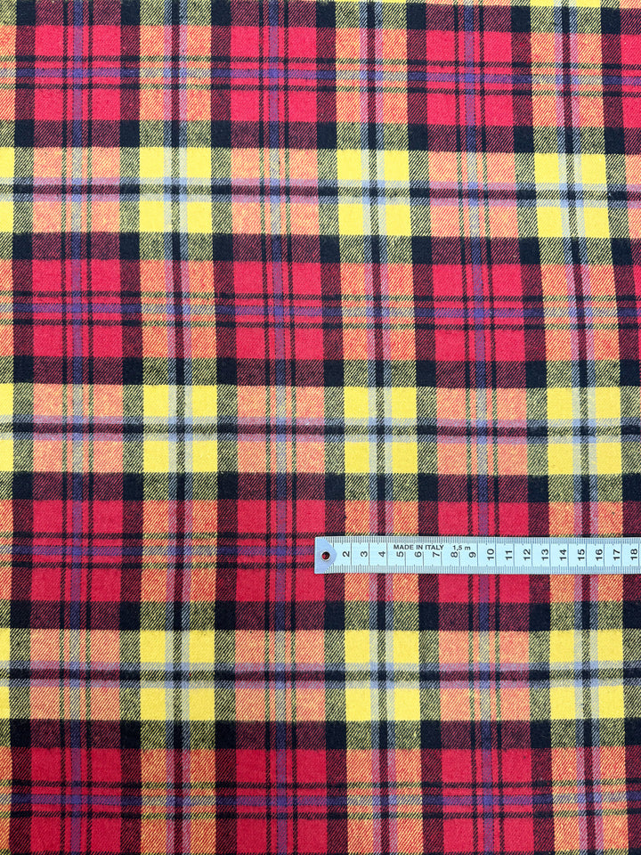 A close-up of Super Cheap Fabrics’ Flannel Tartan - Edinburgh Flame (145cm), featuring red, yellow, and black plaid with a ruler at the bottom right to show the pattern’s scale.