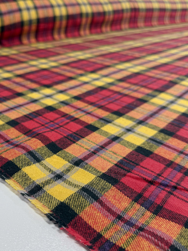 A close-up of Super Cheap Fabrics' Flannel Tartan - Edinburgh Flame (145cm), showcasing its red, yellow, and black plaid pattern with bold texture and intersecting lines for a punk-inspired style.