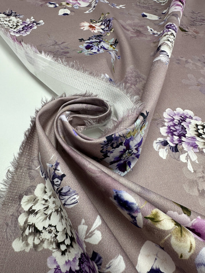 The Cotton Sateen - Shadow Rose from Super Cheap Fabrics features a neatly folded, lightweight purple and white floral pattern with visible frayed edges. The fabric's smooth texture combines with elastane for added stretch, enhancing its versatility and comfort. Width: 120cm.