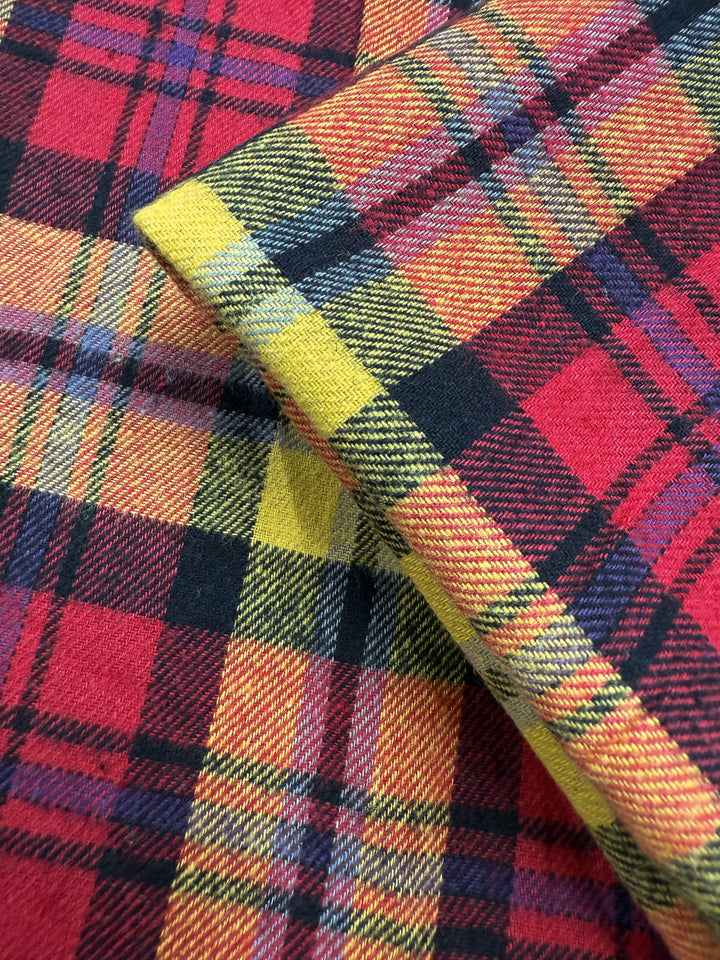 Close-up of Super Cheap Fabrics' Flannel Tartan - Edinburgh Flame (145cm), showcasing its bold red, yellow, black, and white plaid pattern with detailed weave and overlapping folds for a standout punk-inspired style.