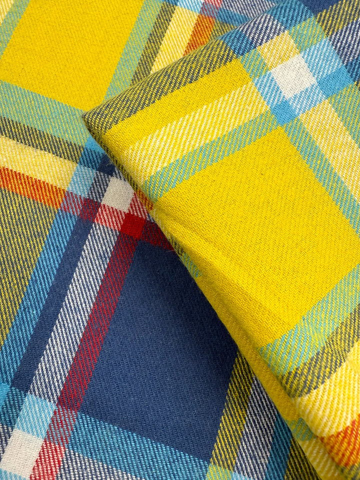 Close-up of Super Cheap Fabrics' Flannel Plaid - Sunshine Heritage (145cm), showing two overlapping pieces with a vibrant plaid pattern in bright yellow, blue, red, white, and green intersecting stripes.