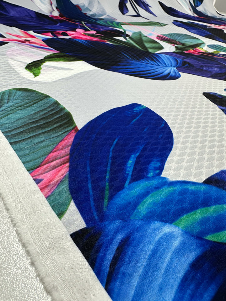 The Super Cheap Fabrics' Textured Poly Sateen - Fawna - 150cm is a vibrant polyester fabric perfect for household décor, featuring a floral pattern with large blue, green, and pink leaves and petals on a smooth, lightweight background.