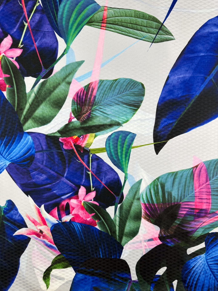 The Super Cheap Fabrics "Textured Poly Sateen - Fawna - 150cm" features a vibrant abstract design with large blue, green, and pink leaves alongside delicate pink flowers on a textured backdrop. Intersecting pastel lines add dynamic visual appeal to this colorful household décor fabric.