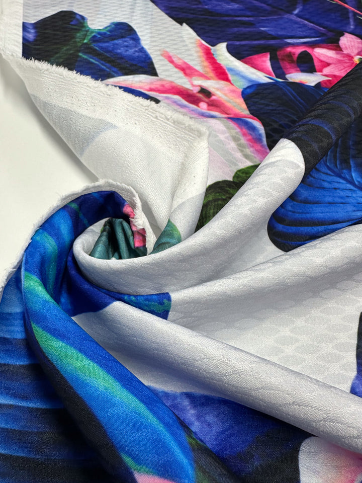 A close-up of Super Cheap Fabrics' Textured Poly Sateen - Fawna, 150cm, shows a vibrant floral print in blue, pink, and green on polyester. The fabric is draped and slightly wrinkled on a white background that enhances the rich colors—ideal for household décor.