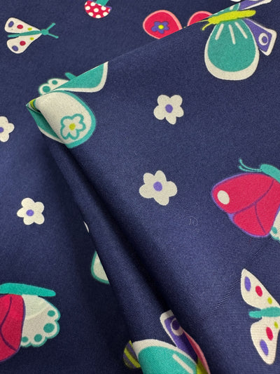 A close-up of the navy blue Printed Delsutered Satin - Butterfly by Super Cheap Fabrics reveals elegant butterfly and flower patterns. This vibrant satin in red, white, and teal hues is perfect for crafting draped dresses into elegant pieces.