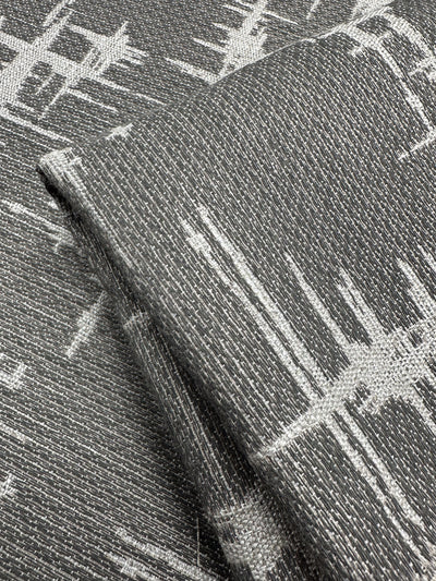 Close-up of Super Cheap Fabrics' Abstract Woven Upholstery - Morissey, 147cm wide: folded gray fabric adorned with white geometric designs. The slightly coarse texture hints at a woven material, featuring contemporary abstract lines and shapes perfect for modern furniture.