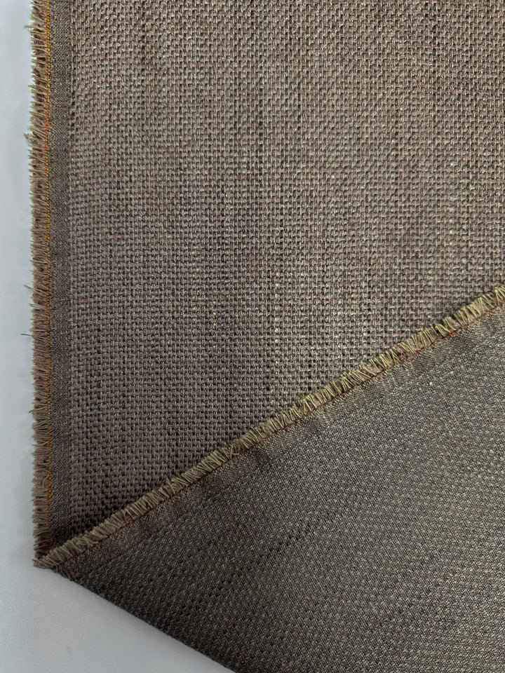 A close-up of Super Cheap Fabrics' Textured Woven Upholstery - Osaka Clay (143cm) displays its brown heavy weave texture with a frayed edge and folded corner revealing the reverse side, set against a plain light background.