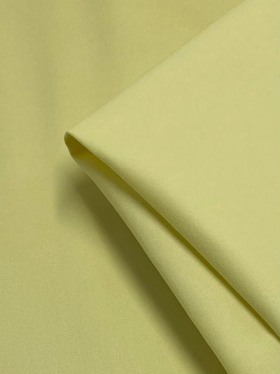 A close-up of Super Cheap Fabrics' Plain Sateen - Banana (145cm) shows smooth, folded light yellow cotton on a matching background. The medium-weight, soft fabric displays its texture and color, perfect for stylish workwear creations.