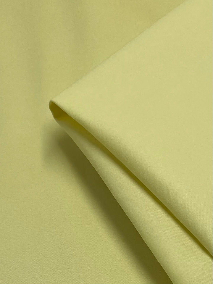 A close-up of Super Cheap Fabrics' Plain Sateen - Banana (145cm) shows smooth, folded light yellow cotton on a matching background. The medium-weight, soft fabric displays its texture and color, perfect for stylish workwear creations.