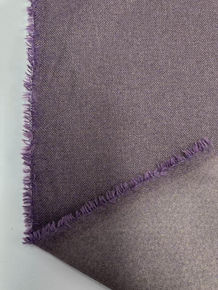 A close-up of Super Cheap Fabrics' Two-Tone Weave Upholstery - Camden Dusk - 145cm shows a dusty purple fabric with a visible weave pattern. The frayed edges on a white background create a delicate, soft border.