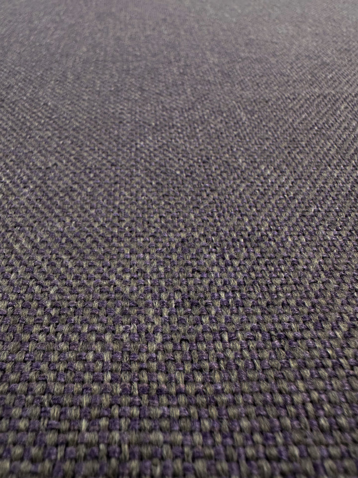 A close-up of the Two-Tone Weave Upholstery - Camden Dusk from Super Cheap Fabrics reveals its textured surface with a grid-like pattern in gray and dusty purple, creating a subtle, intricate design.