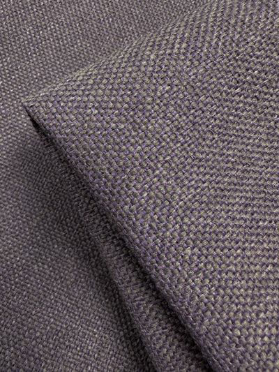A close-up of dark gray, textured upholstery fabric reveals a two-tone weave in dusty purple. A folded section showcases the thickness and texture of Super Cheap Fabrics' Camden Dusk - 145cm.
