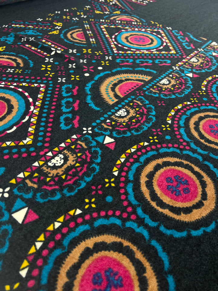 Close-up of the Super Cheap Fabrics Textured Knit Panel - Shapes and Dots (80cm), featuring vibrant blue, pink, yellow, and tan circular and geometric motifs on a black background with a decorative repeating pattern.