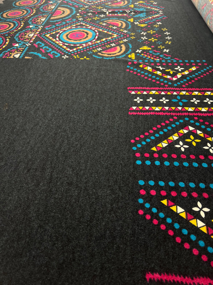 The Super Cheap Fabrics Textured Knit Panel - Shapes and Dots - 80cm features black fabric with vibrant geometric and circular patterns in pink, yellow, blue, and white, displayed diagonally to highlight its unique designs and stretch.