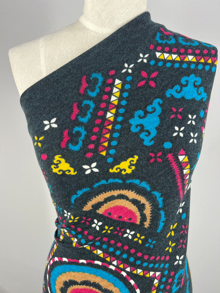 A close-up of a mannequin wearing Super Cheap Fabrics' Textured Knit Panel - Shapes and Dots (80cm), showcasing colorful geometric and abstract patterns in blue, pink, yellow, white, and tan on a dark gray textured knit fabric.