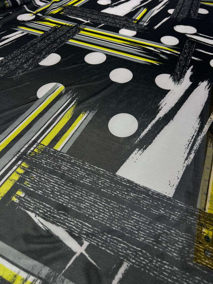 Super Cheap Fabrics' Designer Mesh - Spot & Stripe - 150cm is a lightweight fabric with an abstract geometric design in black, white, and yellow. The pattern includes white polka dots, yellow and black lines, and textured brush strokes. This bold and contemporary design is perfect for fancy dresses, creating a striking visual effect.