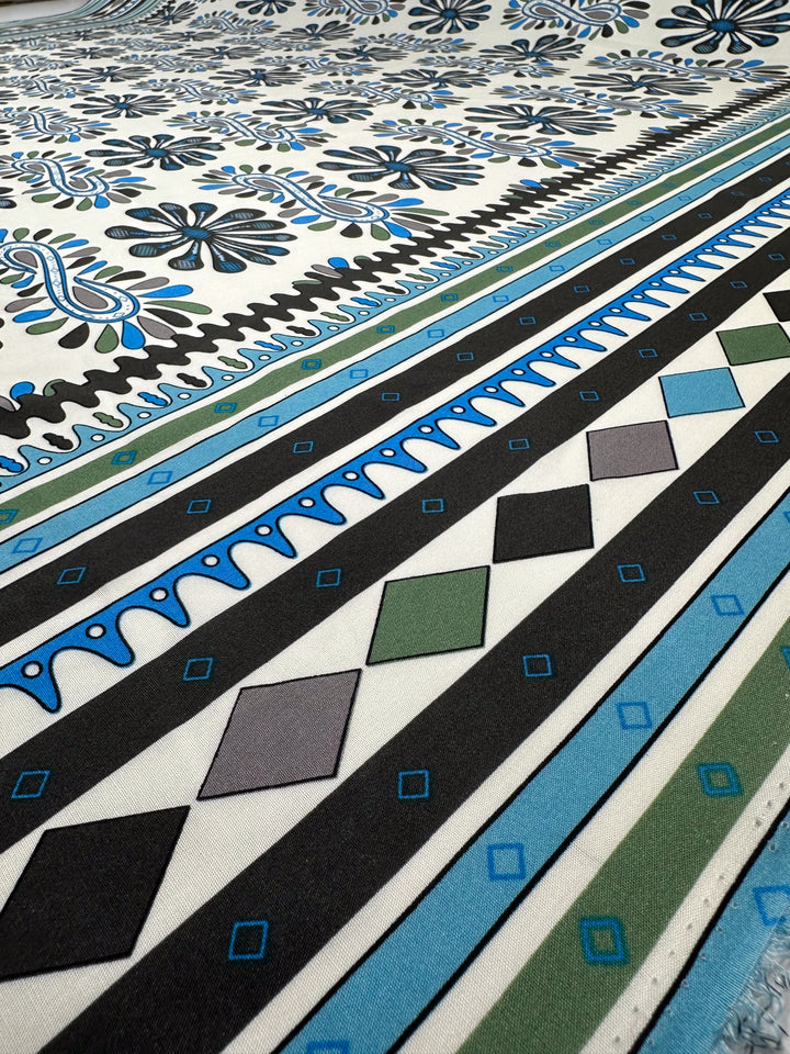 A close-up of Designer Rayon - Dance (145cm) by Super Cheap Fabrics, showcasing lightweight fabric with bold black, blue, green, and gray geometric and floral prints—stripes, diamonds, squares, and stylized flowers.