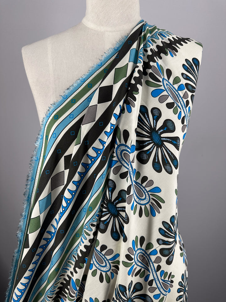 A mannequin displays Designer Rayon - Dance - 145cm from Super Cheap Fabrics, featuring bold geometric and floral patterns in black, blue, and green, with frayed edges and intricate designs for vibrant style.