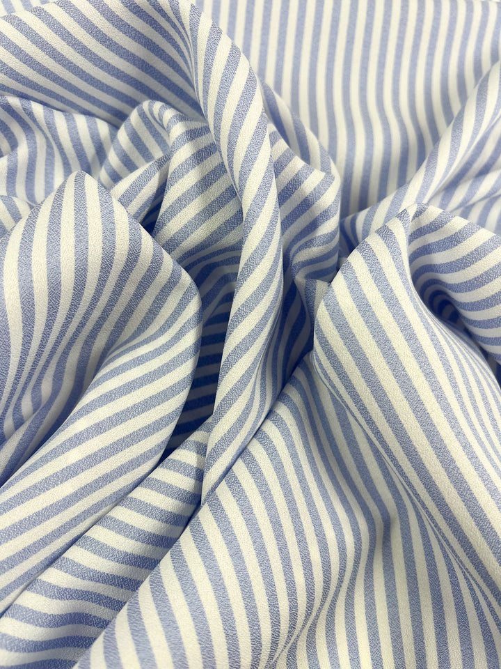 Super Cheap Fabrics' Striped Crepe - Pale Iris (150cm) features light blue and white diagonal and vertical stripes. This lightweight polyester has gentle folds, a soft texture, and drapes elegantly for stylish creations.