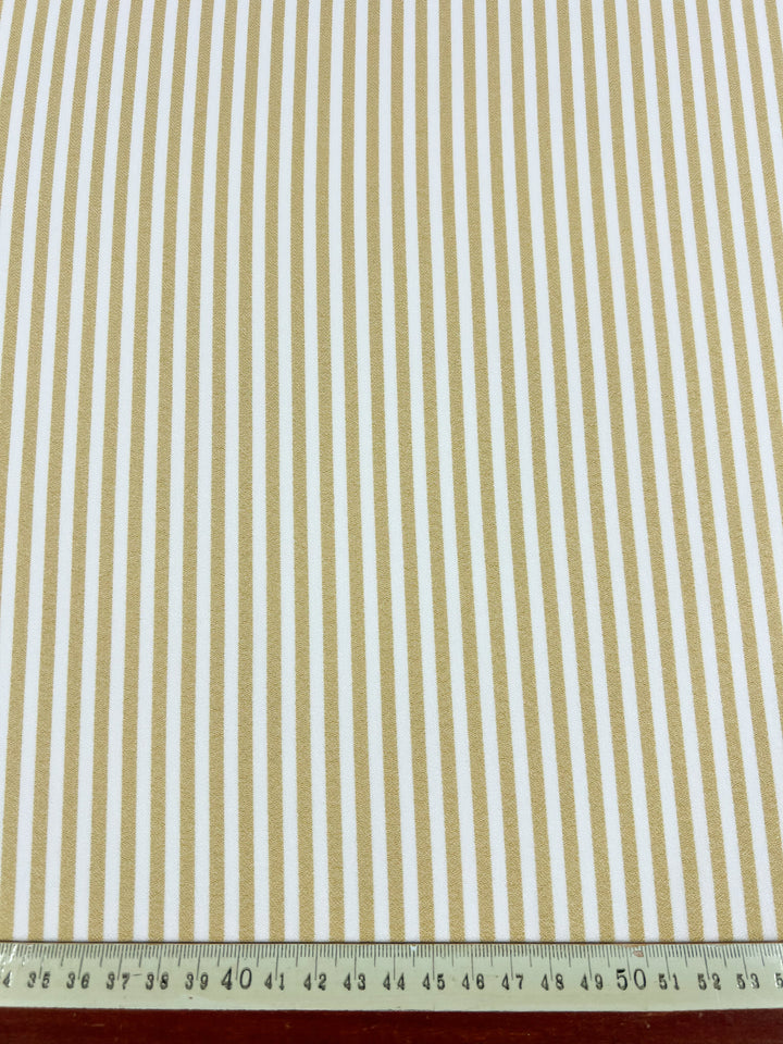 The Super Cheap Fabrics Striped Crepe - Raffia - 150cm, a lightweight polyester fabric with vertical beige and white stripes, is displayed with a metal ruler at the bottom to show stripe width and overall scale.