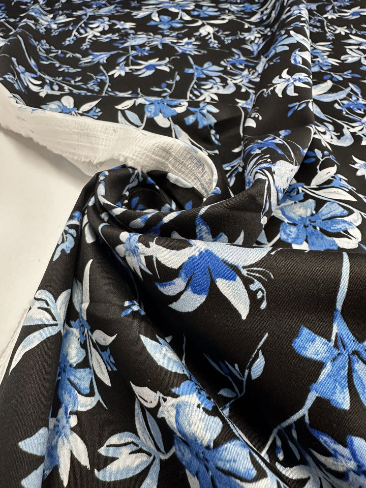 Super Cheap Fabrics' Cotton Sateen - Blue Lotus (146cm) is a medium weight fabric featuring large blue and white lotus flowers with light blue leaves, displayed partially rolled and spread out on a white surface.