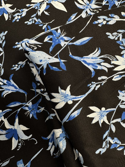 A close-up of Super Cheap Fabrics’ Cotton Sateen - Blue Lotus (146cm), a medium weight cotton spandex blend in black-blue, features blue and white lotus floral patterns with gentle creases and subtle folds.