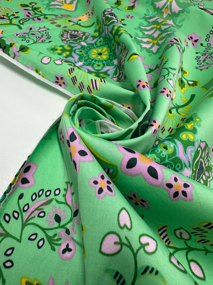 A close-up of Super Cheap Fabrics’ Cotton Sateen - Lime Mosaic (145cm), featuring whimsical floral and nature-inspired patterns in pink, yellow, white, and black—perfect for household décor.