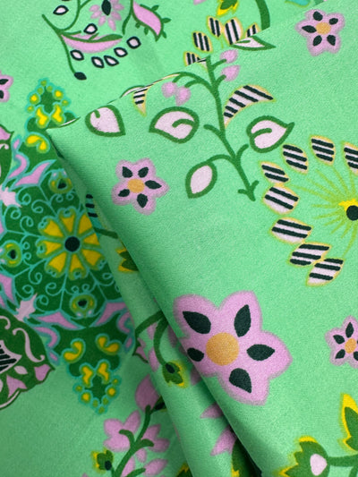 Close-up of Cotton Sateen - Lime Mosaic by Super Cheap Fabrics (145cm), showing vibrant pink, yellow, black, and white floral and geometric patterns on a green background—perfect for stylish home décor.