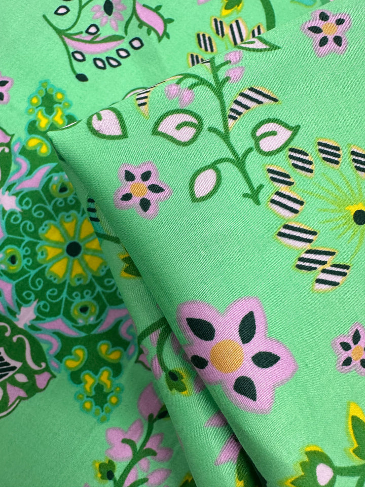 Close-up of Cotton Sateen - Lime Mosaic by Super Cheap Fabrics (145cm), showing vibrant pink, yellow, black, and white floral and geometric patterns on a green background—perfect for stylish home décor.