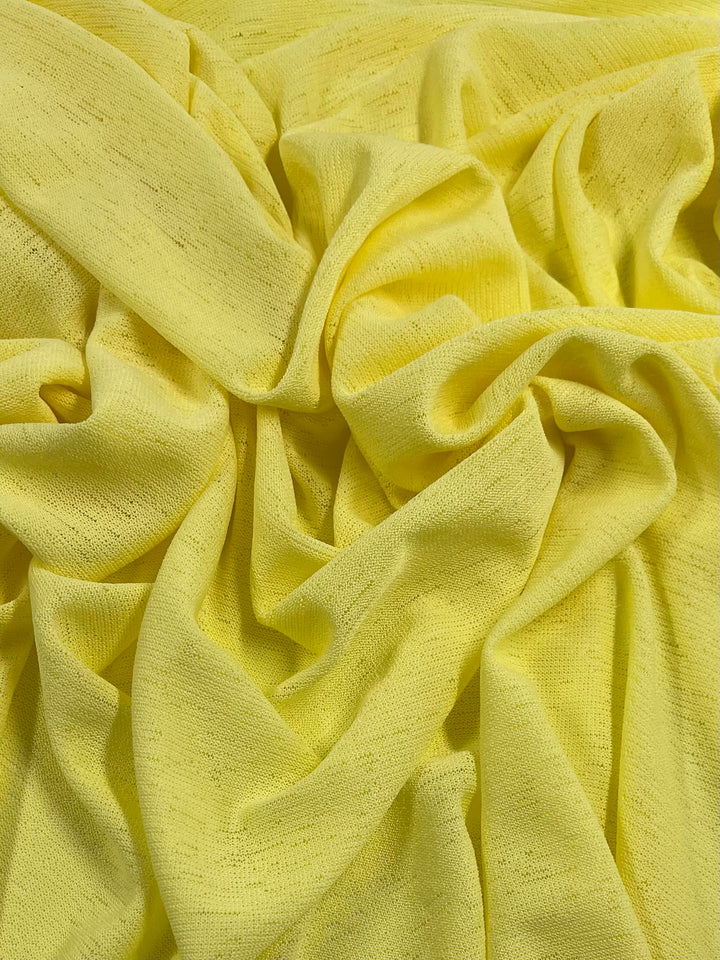 A close-up image of the Lightweight Slub Jersey - Lemon from Super Cheap Fabrics, showcasing its light, slightly sheer texture with visible tiny holes. The fabric is bunched up in soft folds, highlighting its smooth and flowy nature—ideal for creating dresses and tops made from textured knit fabrics.