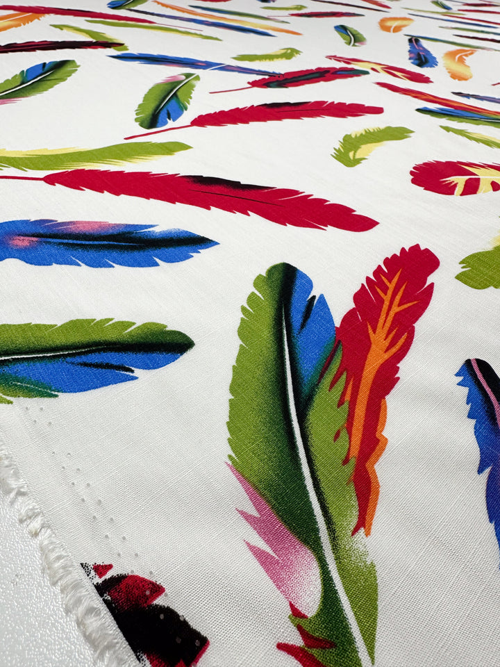 A close-up of Super Cheap Fabrics' Bamboo Rayon - Feather White (150cm), showcasing its visible texture and vibrant red, green, blue, and yellow feather pattern—ideal for beginner sewing projects.