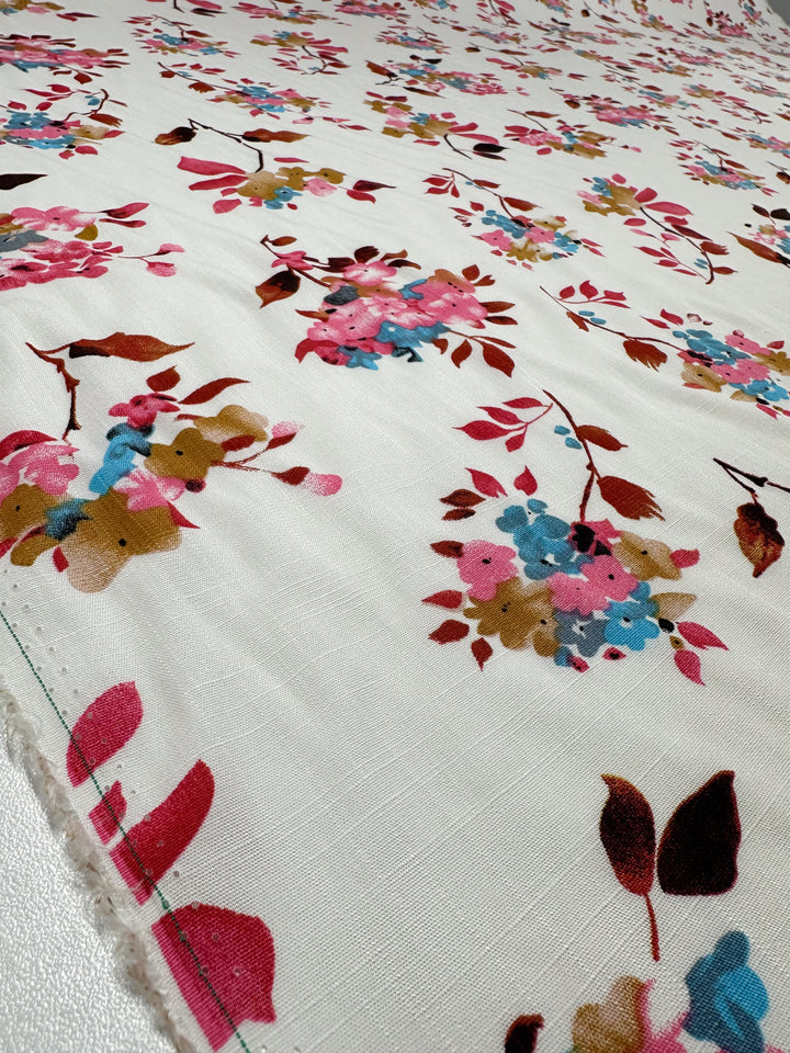 A close-up of Super Cheap Fabrics' Bamboo Rayon - Lil Flower (150cm), a lightweight cream-colored fabric with a subtle weave, showcasing repeating floral clusters in pink, blue, and brown—perfect for versatile multi-use projects.
